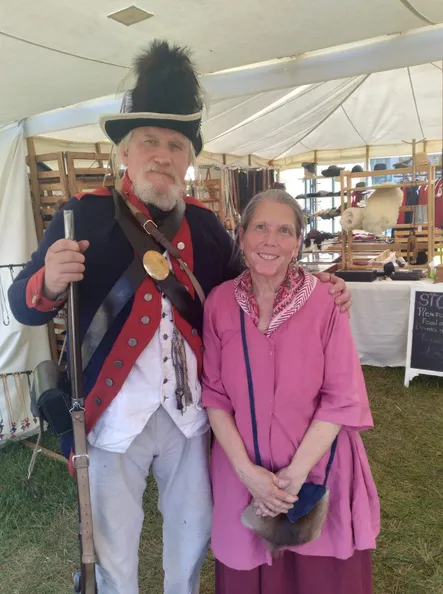 Kacey and Kathy Crager standing inside their sutler's tent, Kacey in a Continental uniform and Kathy in a rose-colored dress
